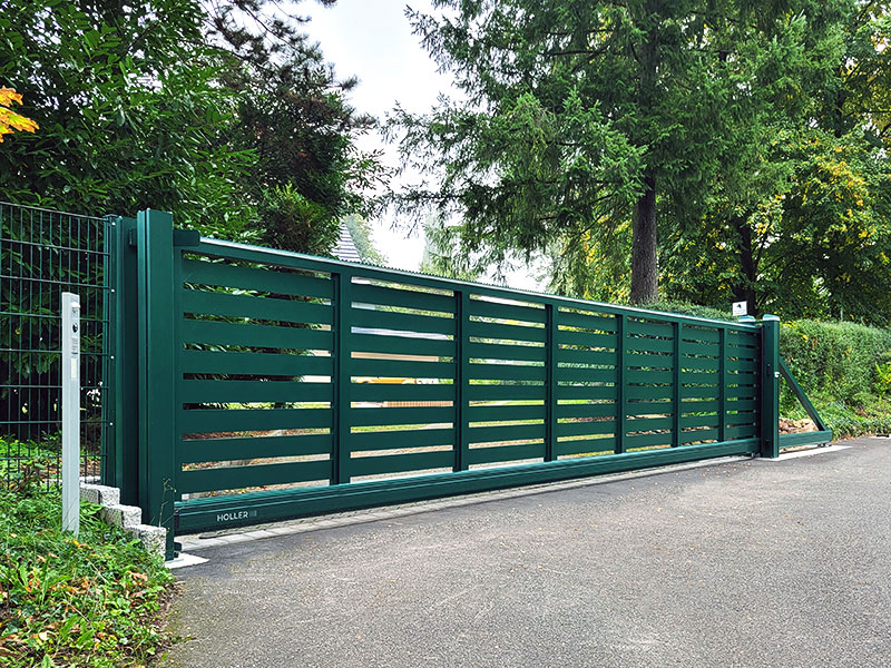 Portail coulissant Holler vert foncé entouré par la nature et les arbres